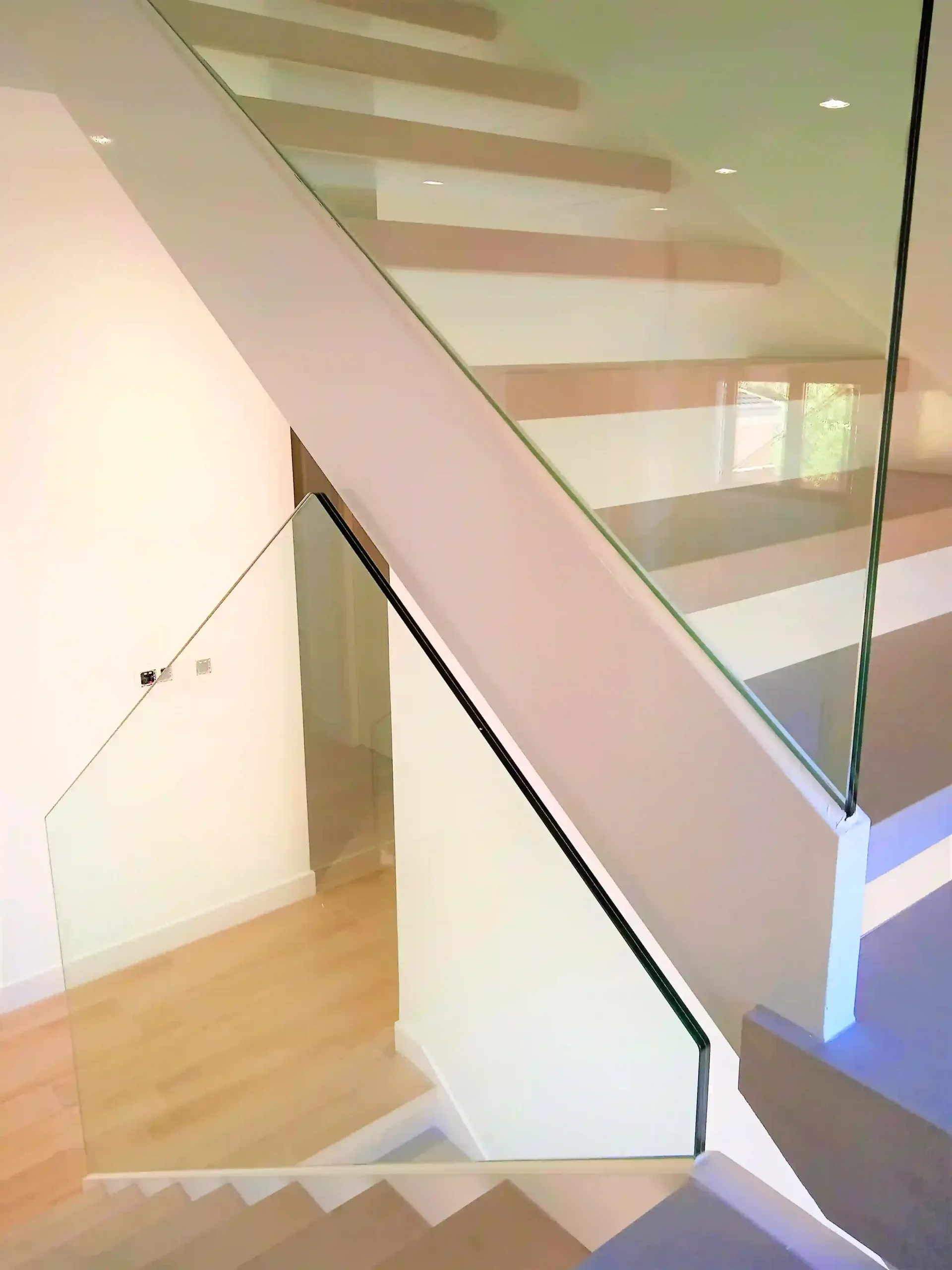 Una escalera con barandilla de cristal y escalones de madera.