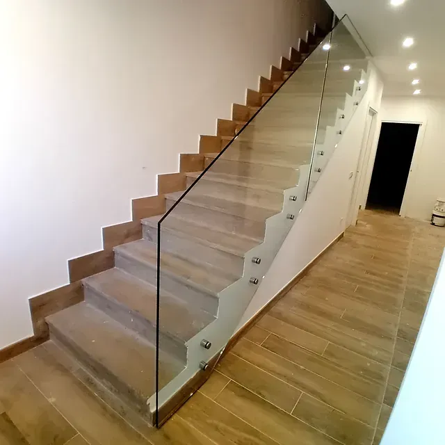 Una escalera con barandilla de cristal en un pasillo.