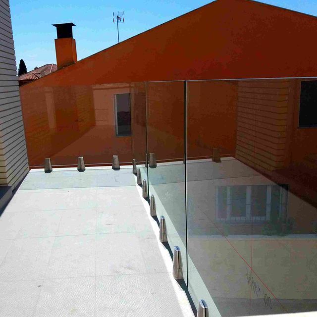 Un balcón con barandilla de cristal y un edificio naranja al fondo.