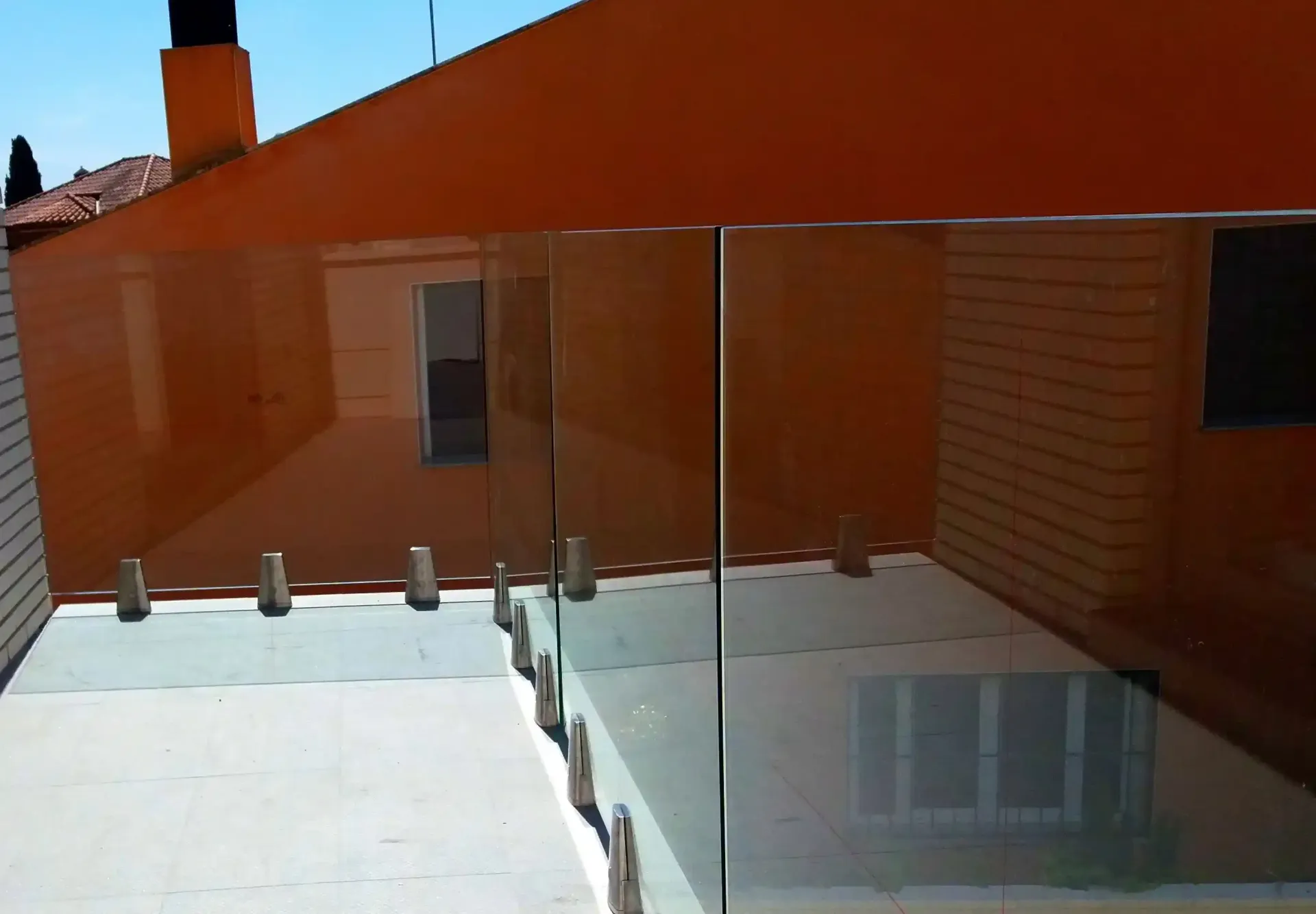 Un balcón con barandilla de cristal y un edificio al fondo.