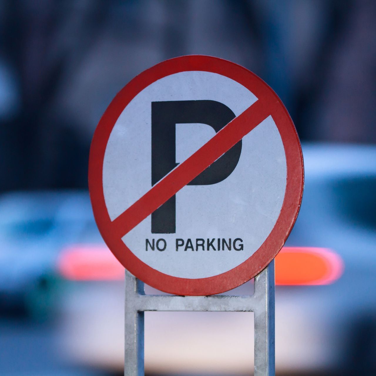 Una señal de no estacionar con un automóvil al fondo
