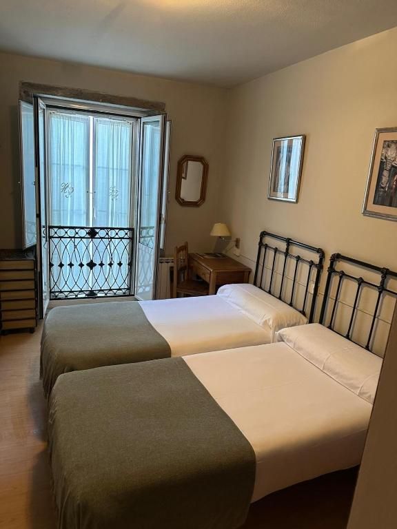 Un dormitorio con dos camas, un escritorio, un espejo y un balcón.