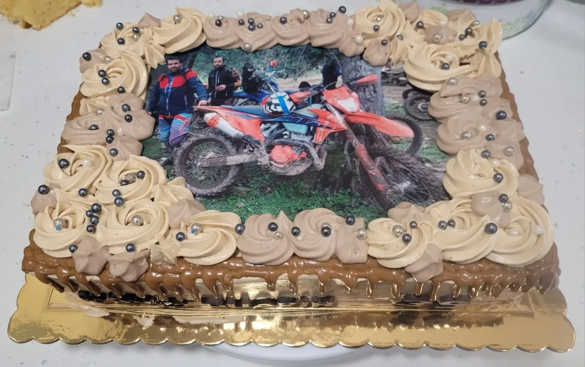 Tarta cuadrada con cobertura de chocolate y una foto de un piloto de motocross en la parte superior, decorada con espirales y perlas