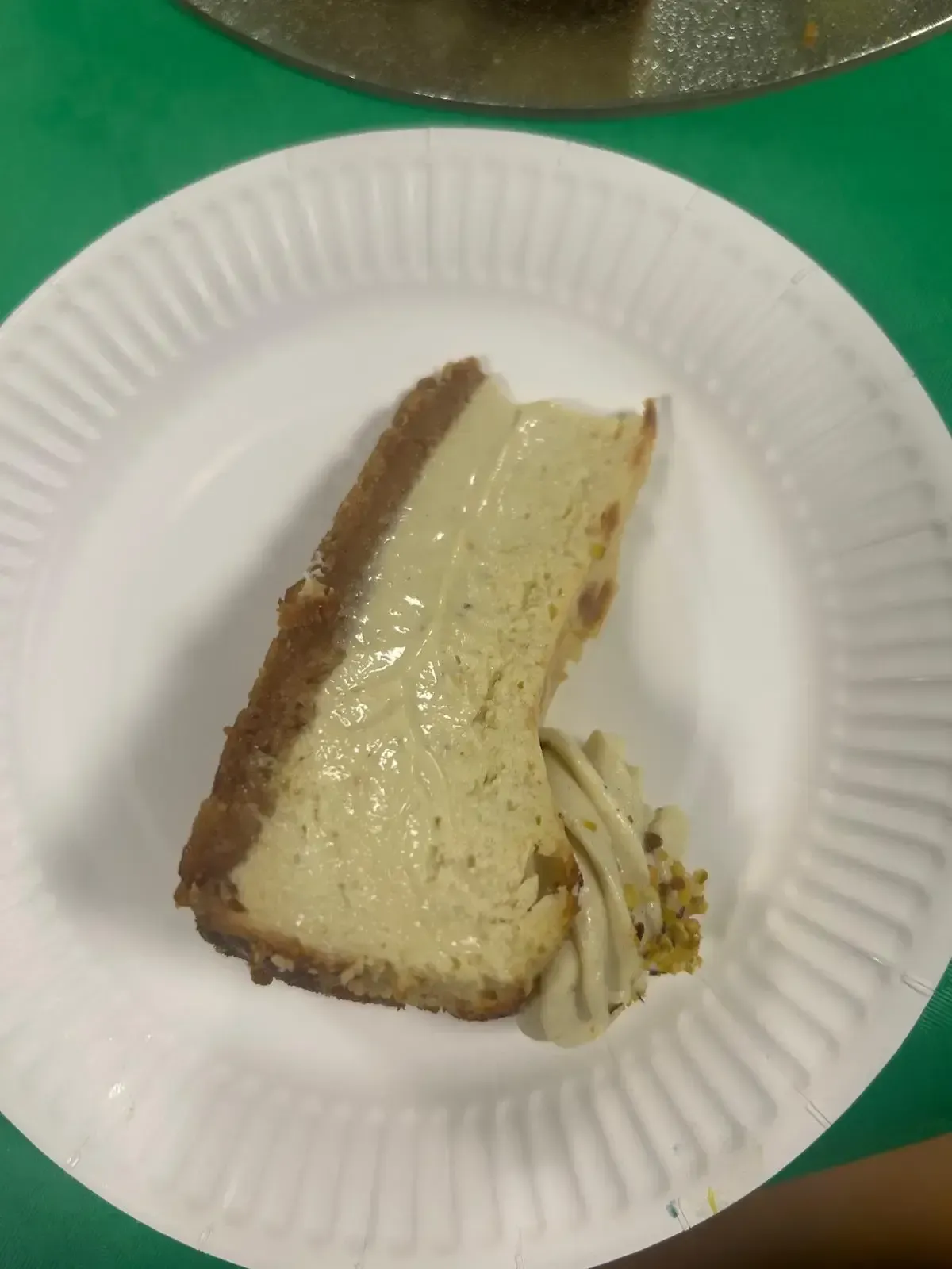 Porción de tarta en un plato de papel blanco con un tenedor pequeño sobre una mesa verde