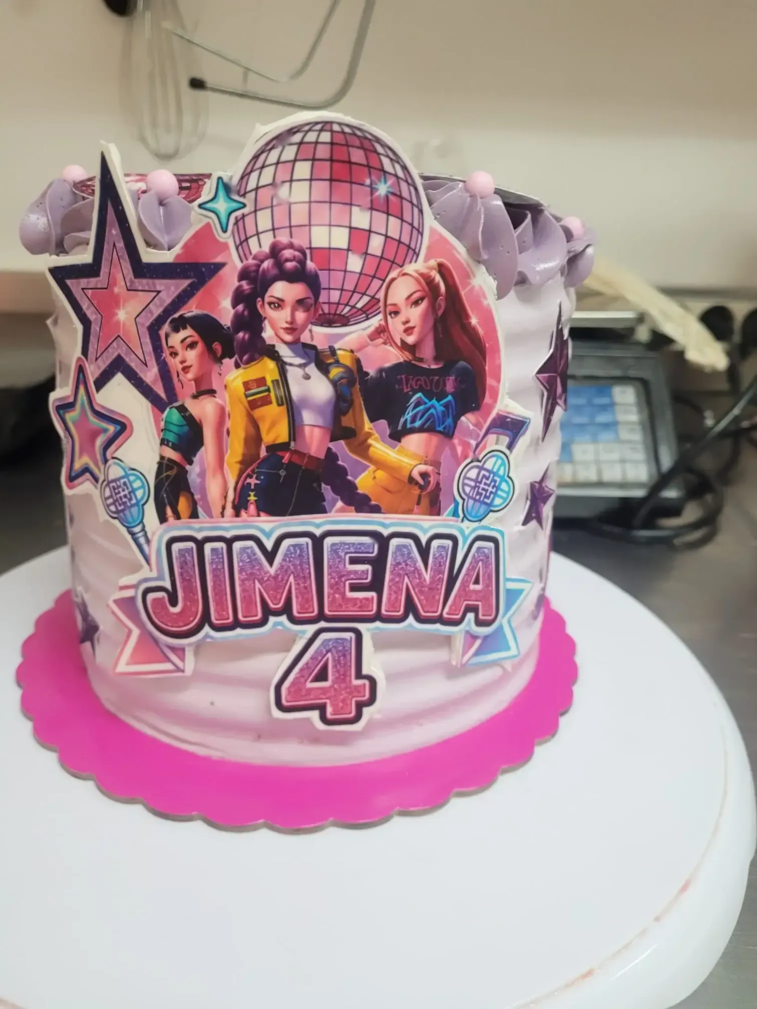 Tarta de cumpleaños con un adorno rosa de estilo disco que dice «Jimena 4», sobre un soporte blanco