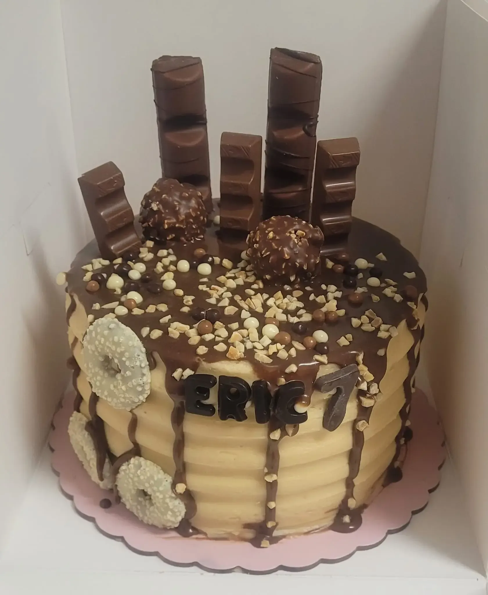 Pastel de chocolate con cobertura de chocolate, barritas apiladas y adornos de caramelo blanco sobre una base rosa