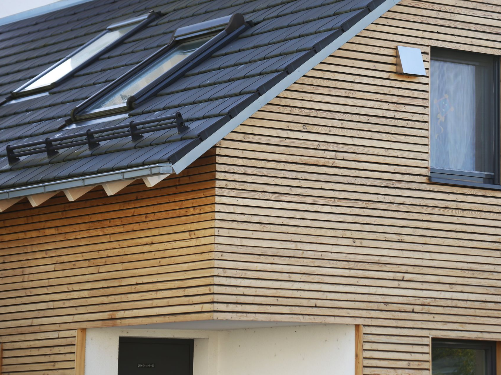 Extérieur de maison moderne avec toit de tuiles foncées et bardage en bois clair.