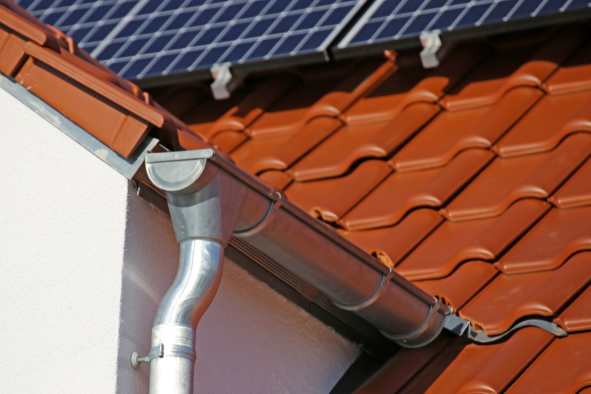 Des panneaux solaires et un toit de tuiles rouges avec une gouttière et une descente pluviale sur une maison