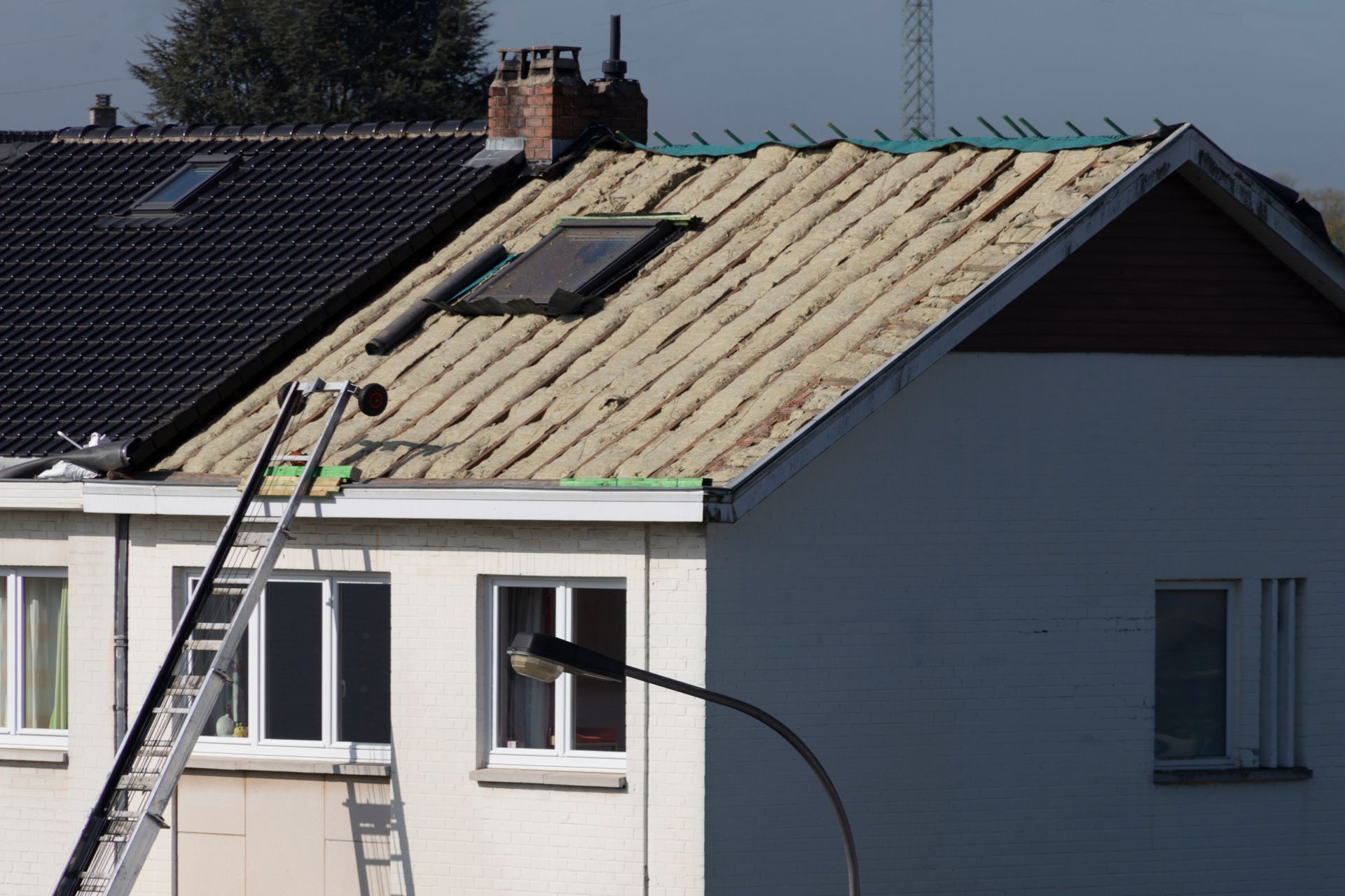 Toiture en réparation, une échelle appuyée contre une maison à côté d'une toiture partiellement décapée.