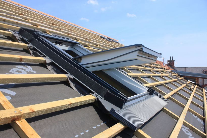 Toiture en construction avec liteaux de bois apparents et solins métalliques pour puits de lumière sur une toiture en pente