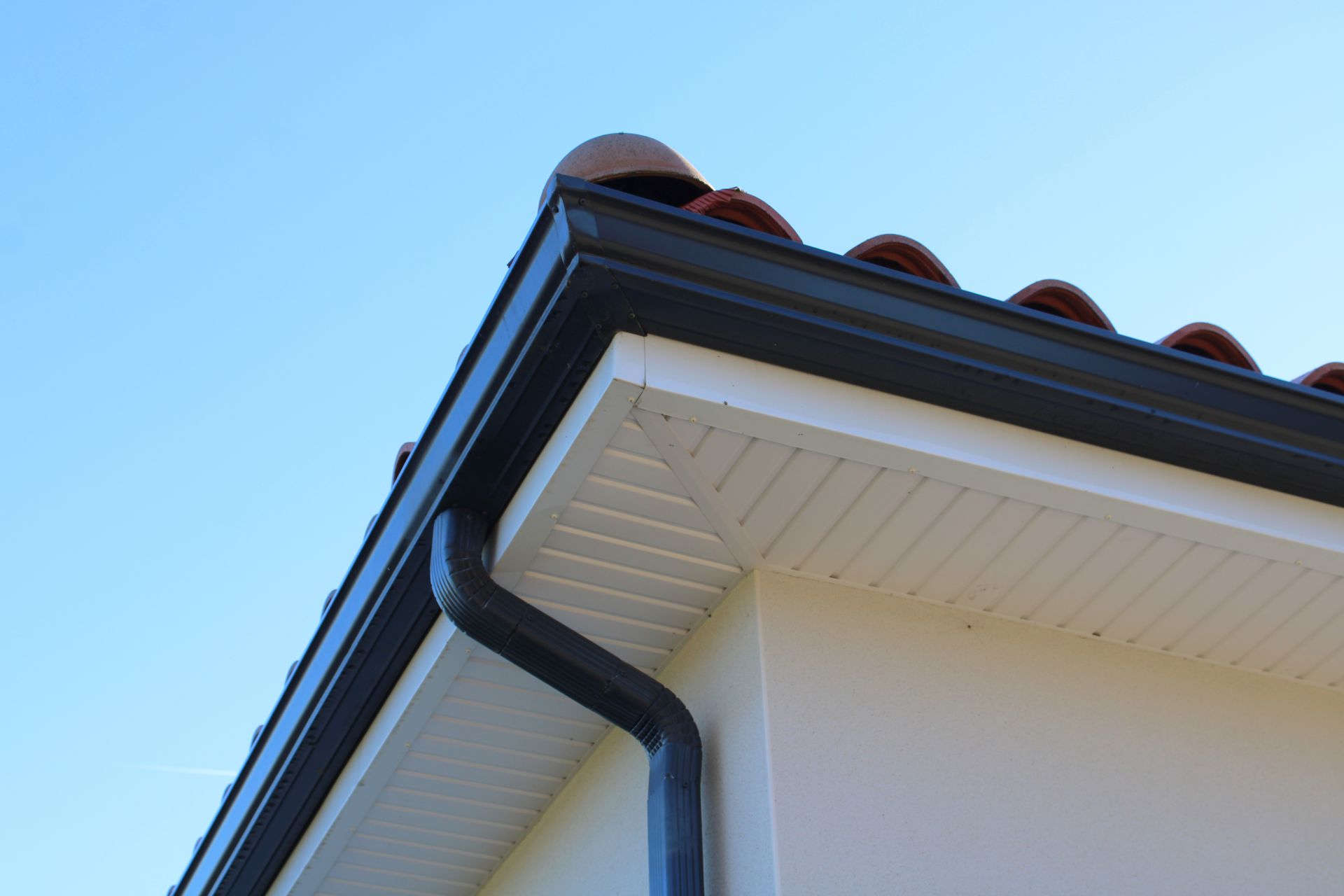 Gros plan sur le toit d'une maison blanche aux boiseries sombres et aux tuiles rouges se détachant sur un ciel bleu.