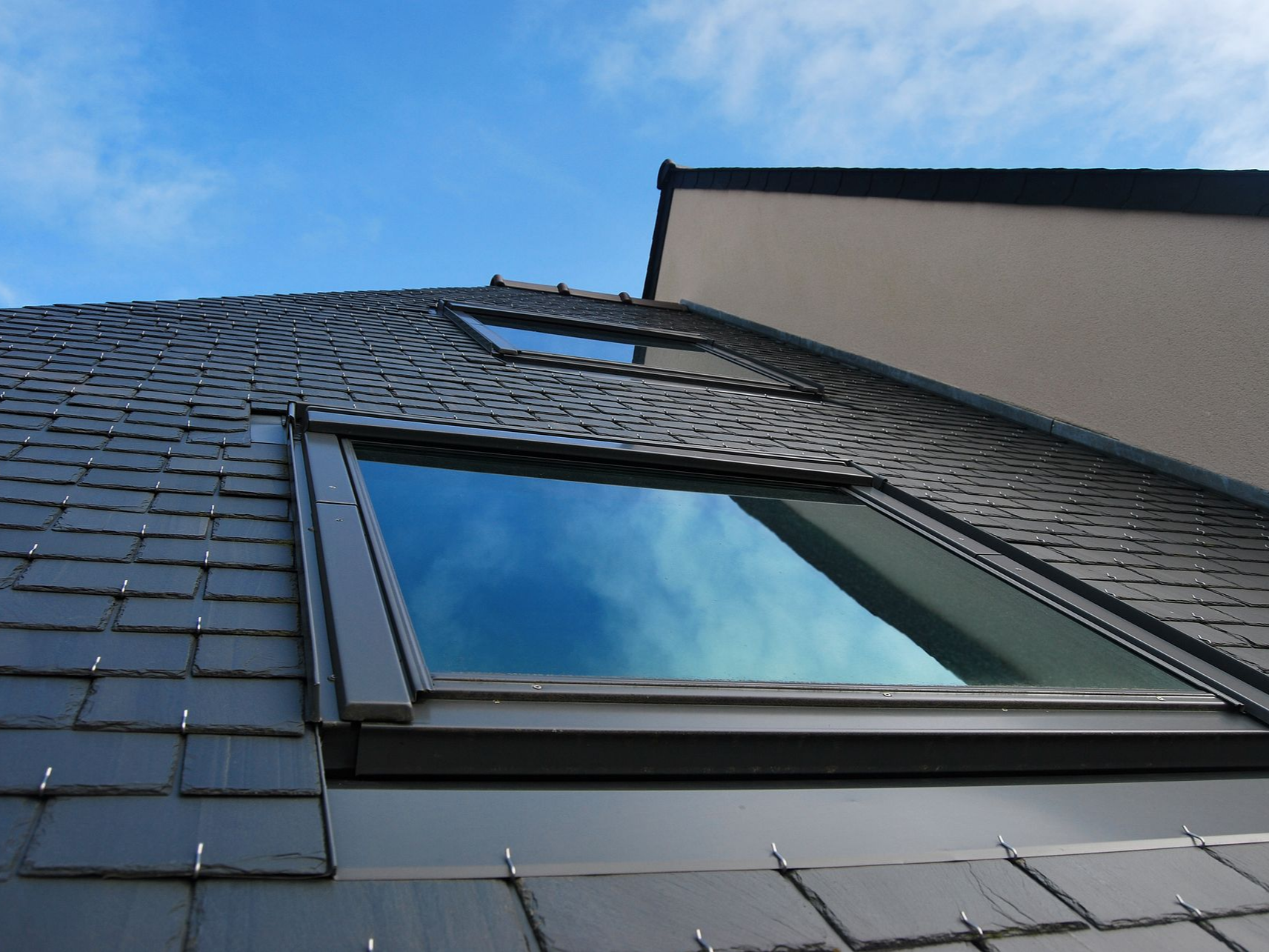 Puits de lumière sur le toit d'une maison aux bardeaux sombres sous un ciel bleu