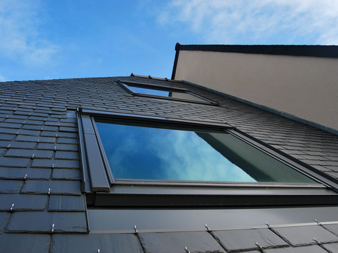 Puits de lumière sur le toit d'une maison aux bardeaux sombres sous un ciel bleu
