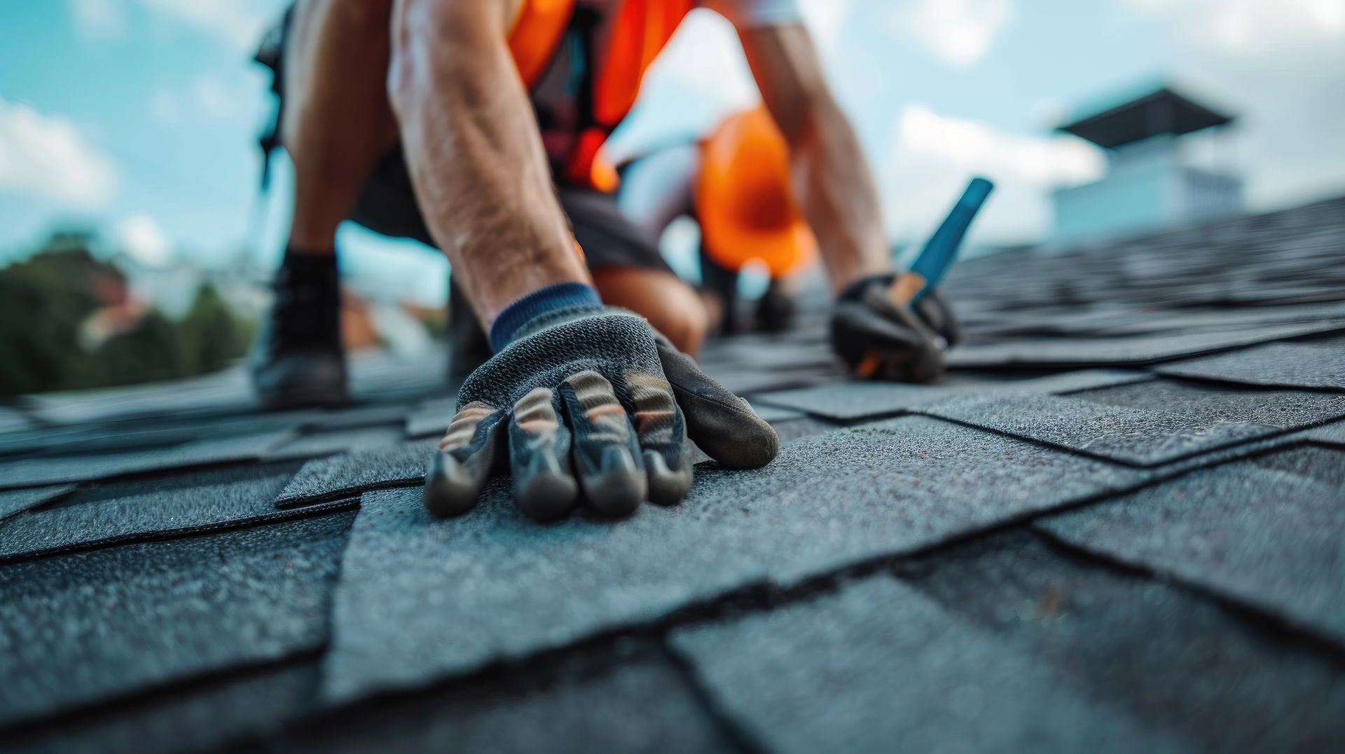 Un ouvrier en gilet orange pose des bardeaux de toiture avec des gants à l'extérieur