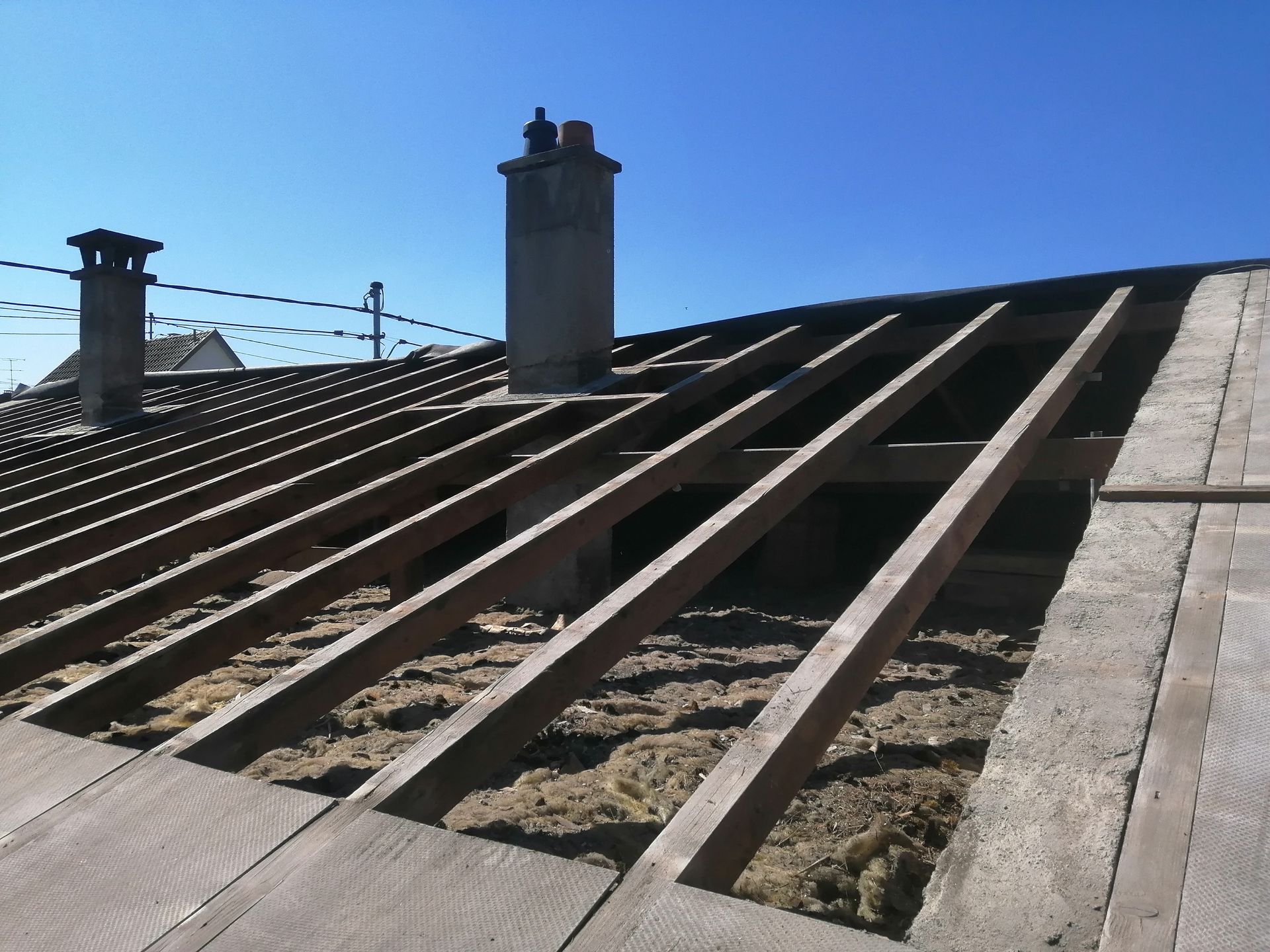 Toiture en construction avec poutres en bois apparentes, cheminées et isolation sous un ciel bleu