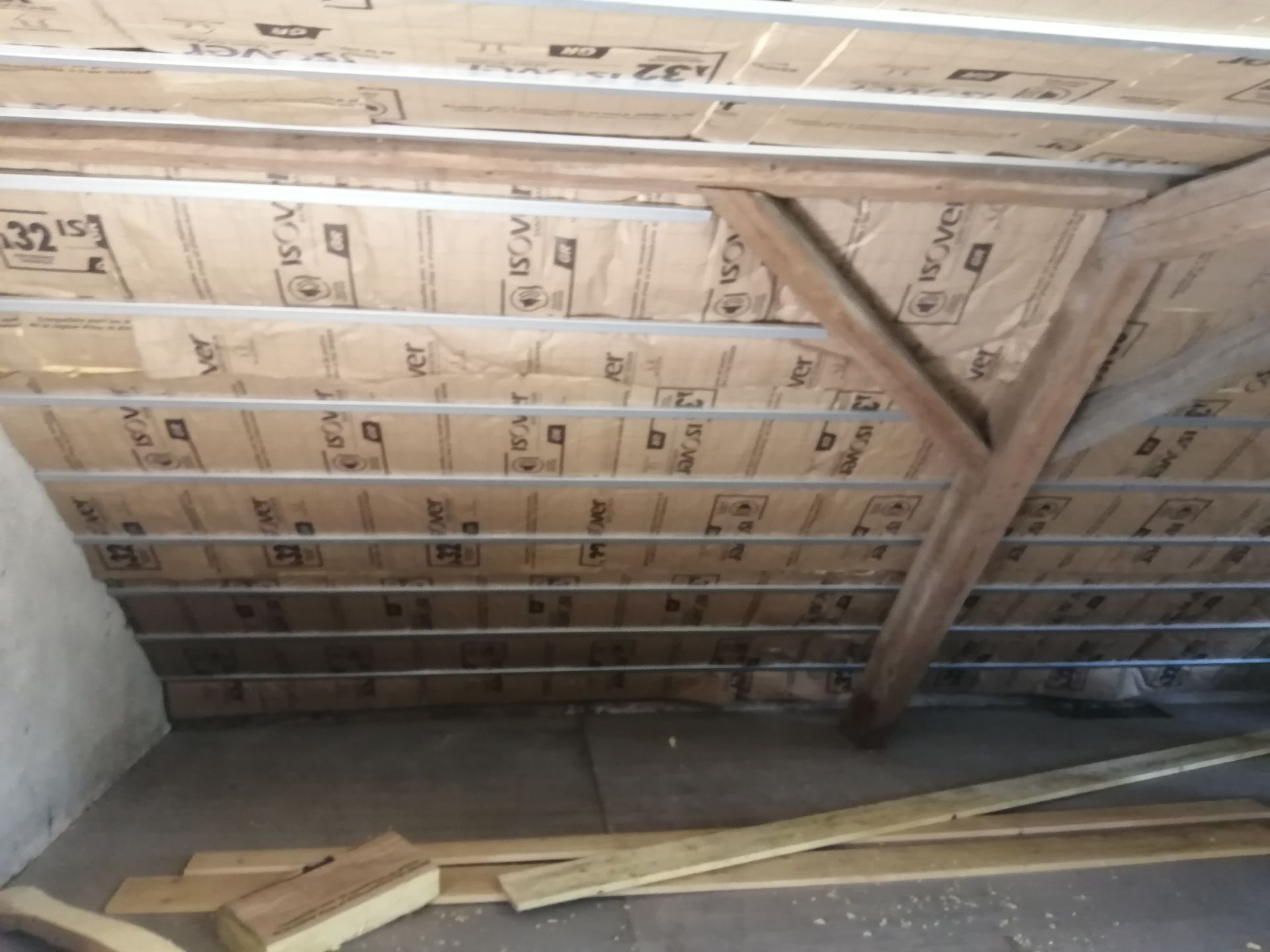 Charpente du plafond du grenier avec isolation et planches de bois éparses au sol
