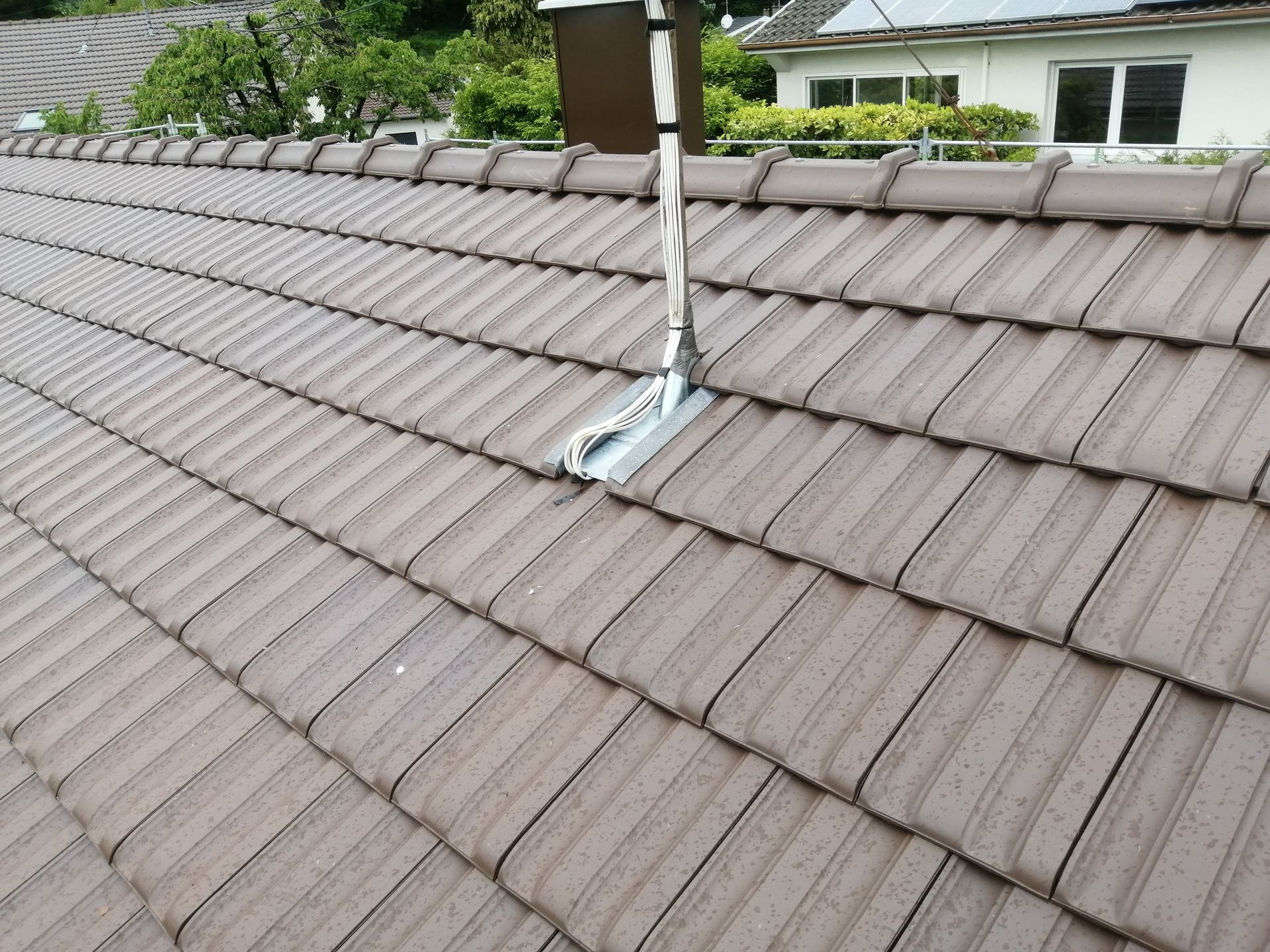 Toiture avec un solin de ventilation blanc sur des tuiles grises, montrant une section réparée près du faîtage