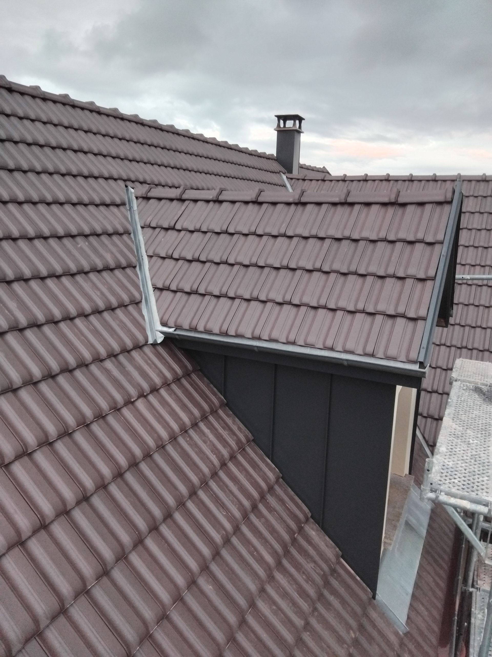 Toits de tuiles brunes autour d'une cour étroite avec une cheminée et un ciel gris couvert