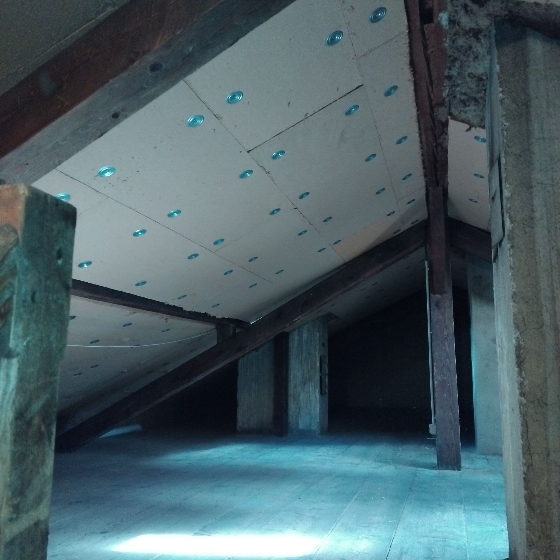 Grenier intérieur avec panneaux d'isolation blancs inclinés, poutres apparentes et sol en béton en construction.
