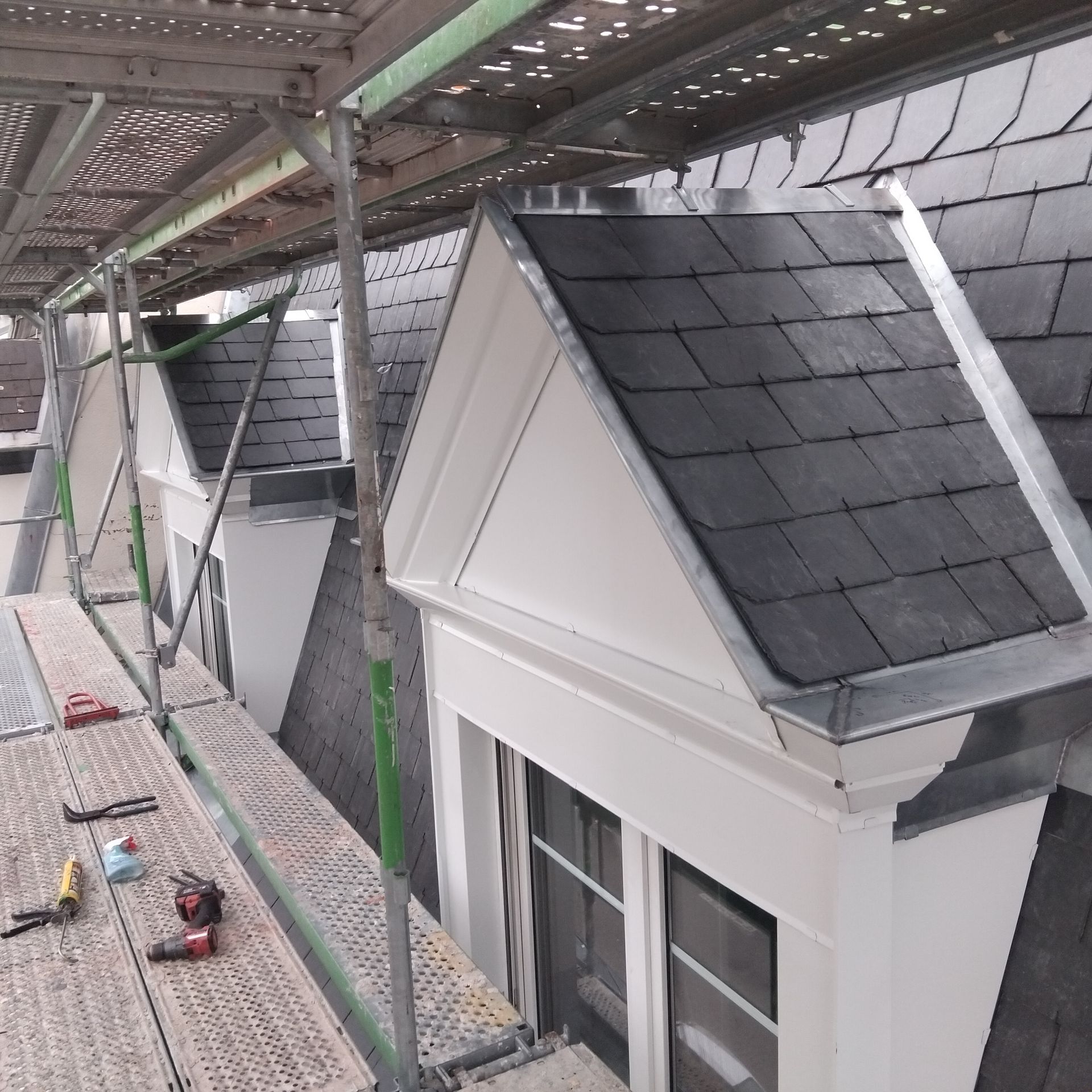 Échafaudages à côté des lucarnes d'une maison en construction, avec des outils de chantier sur la plateforme.