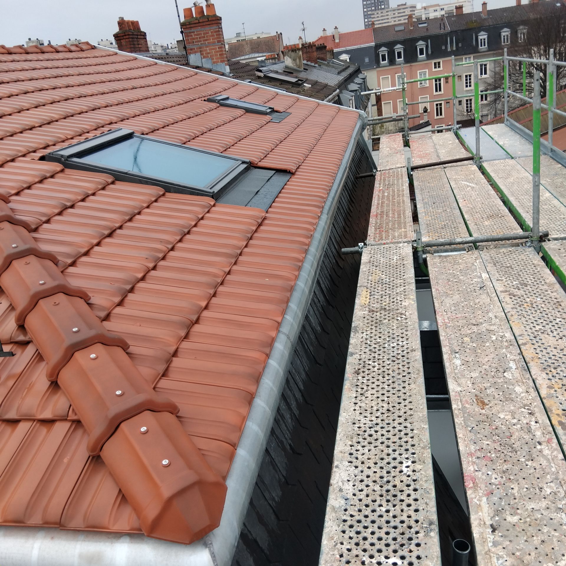 Toit-terrasse avec tuiles rouges, puits de lumière et échafaudages donnant sur des immeubles d'appartements voisins