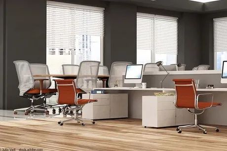 Modernes Großraumbüro mit weißen Schreibtischen, ergonomischen Stühlen und großen Fenstern.