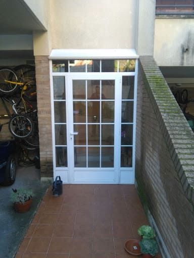 Puerta con marco blanco y múltiples paneles de vidrio; camino de baldosas rojas; paredes beige; bicicletas a la izquierda.