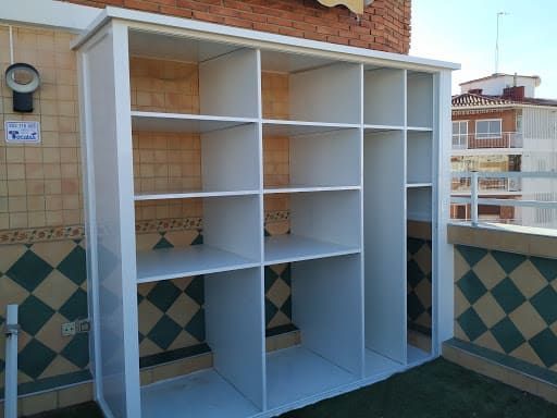 Estantería blanca con múltiples compartimentos sobre un patio embaldosado.