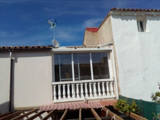 Balcón con columnas blancas y puertas corredizas de vidrio, antena parabólica, cielo azul.