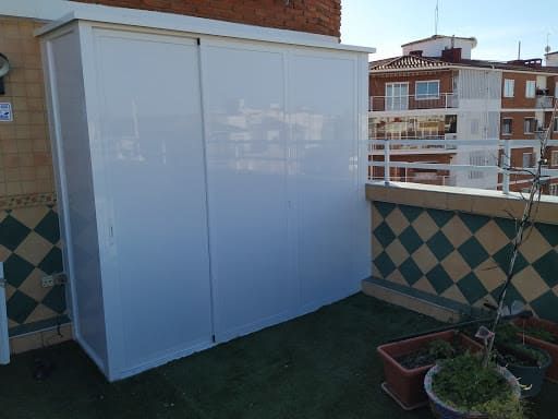 Armario de almacenamiento blanco en un balcón en la azotea con azulejos a cuadros verdes y negros, cerca de plantas en macetas.