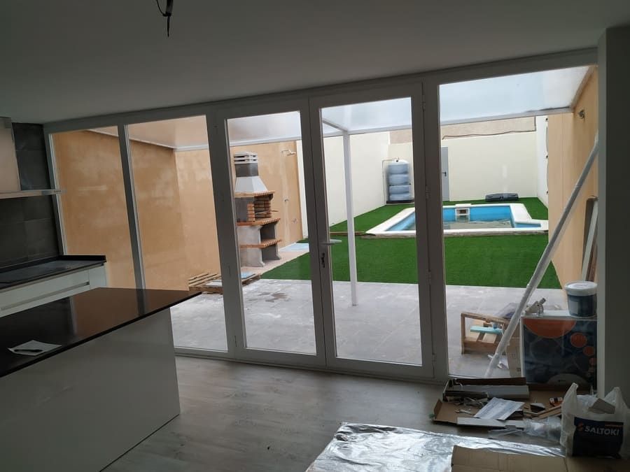 Vista interior de una cocina con grandes puertas de vidrio que se abren a un patio trasero con piscina y zona de barbacoa.