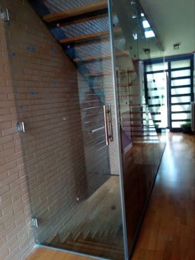 Puerta de vidrio y escalera en una casa moderna, con pisos de madera y pared de ladrillo visibles.