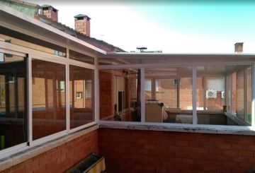 Patio acristalado con marcos blancos, anexo a un edificio de ladrillo. Día soleado y luminoso.