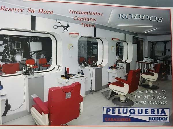 Interior de una barbería moderna de color rojo y blanco con espejos, sillas y puestos de peluquería.