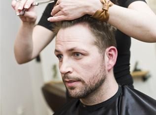 Peluquero recortando el cabello de un hombre con tijeras en un salón de belleza.