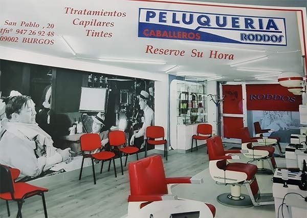 Interior de una peluquería con sillas rojas y un gran letrero de