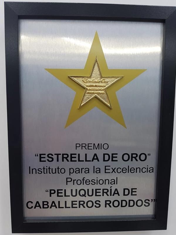 Framed gold star plaque with Spanish award text for “Estrella de Oro” and “Peluquería de Caballeros Rodos”