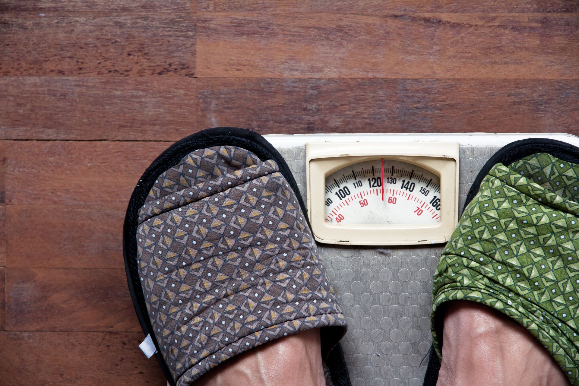 Pies en pantuflas sobre una báscula de baño, registrando peso.