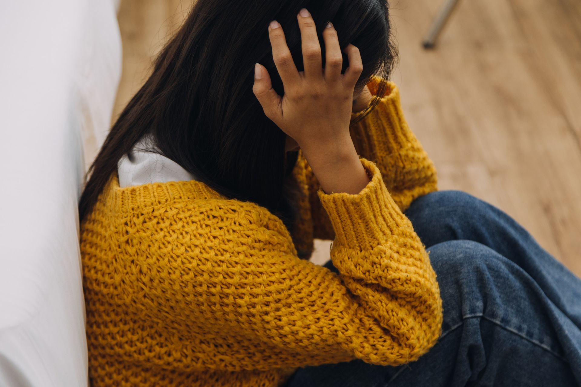 Mujer sentada en el suelo, con la cabeza entre las manos, suéter amarillo y aspecto angustiado.