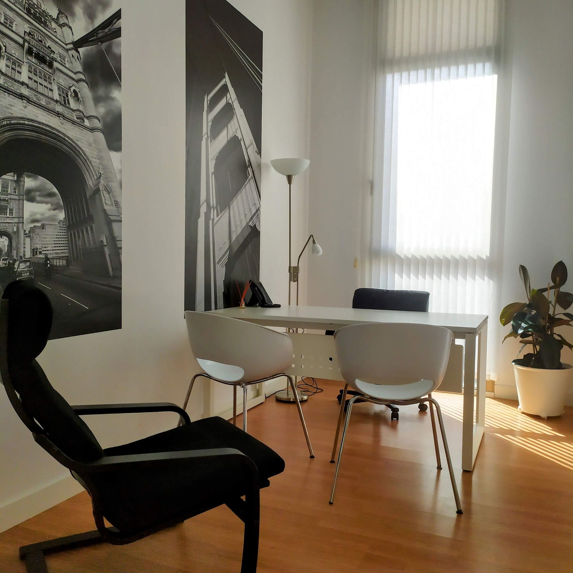 Oficina con escritorio, sillas, ventana grande y arte urbano en blanco y negro.