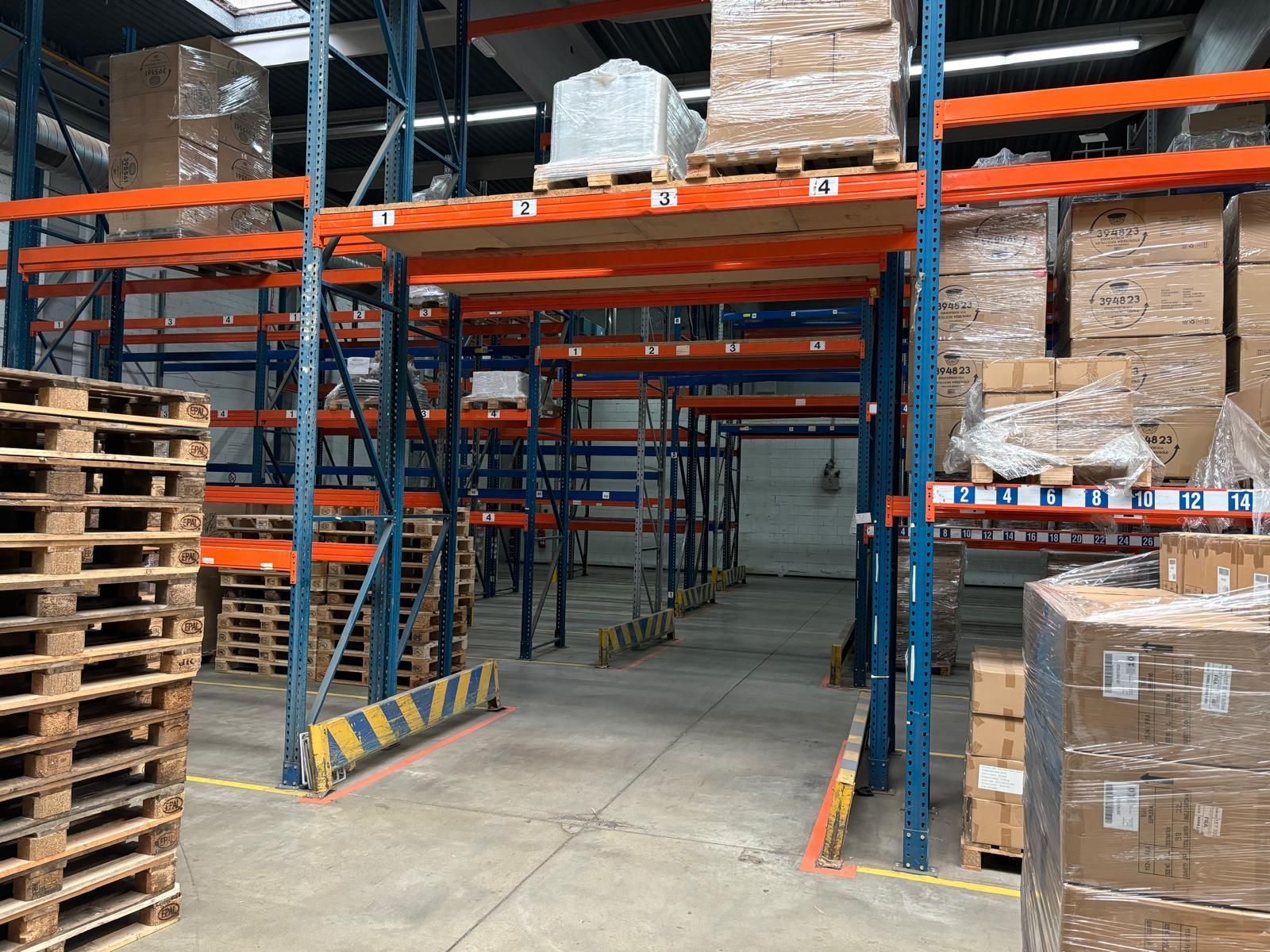 Lagerinnenraum mit Metallregalen für Paletten und Kisten; Gang mit gelben Streifen markiert.