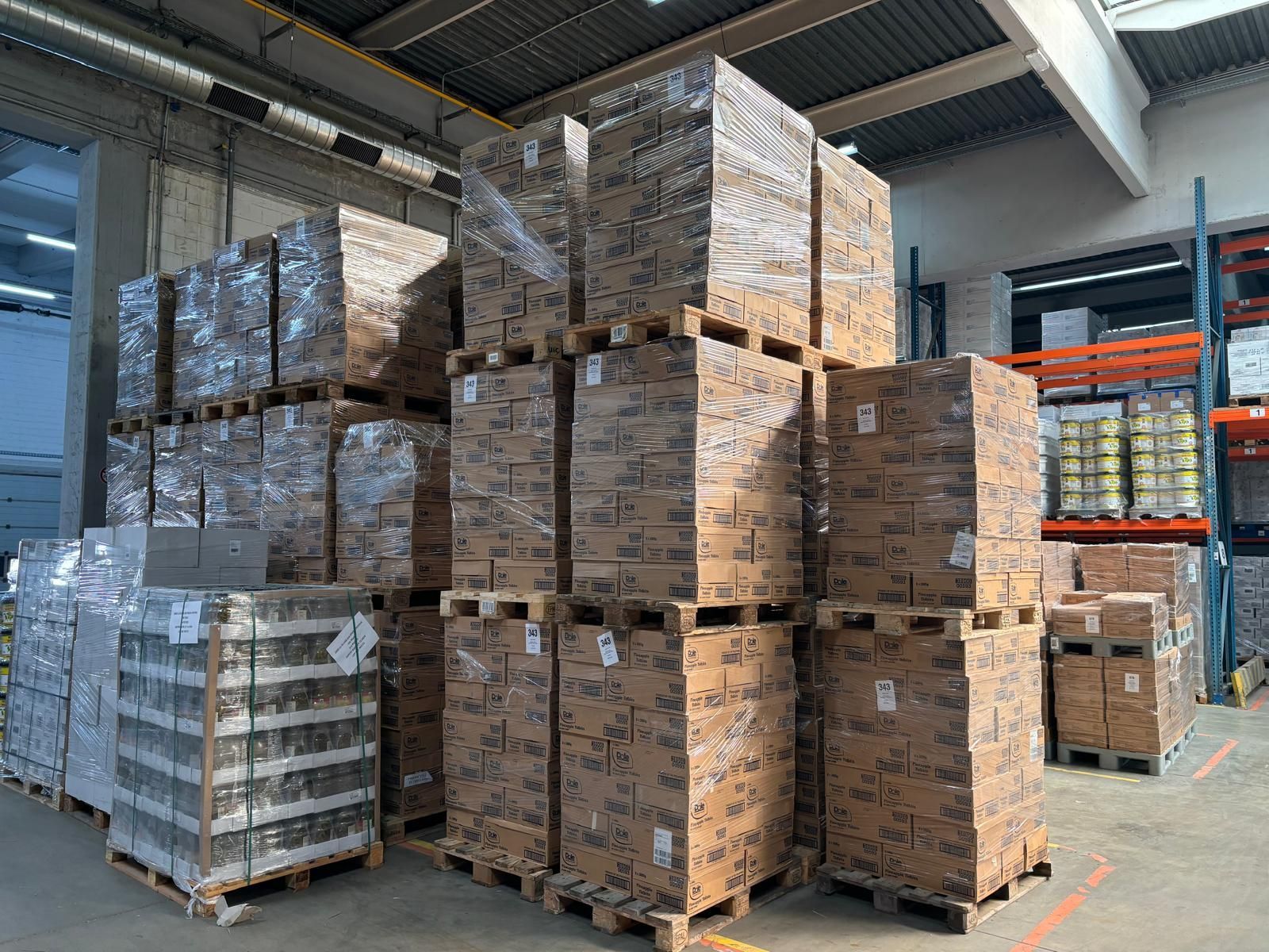 Paletten mit verpackten Waren in einem Lagerhaus, hoch gestapelt. In durchsichtige Plastikfolie eingewickelte Kartons im Innenbereich.