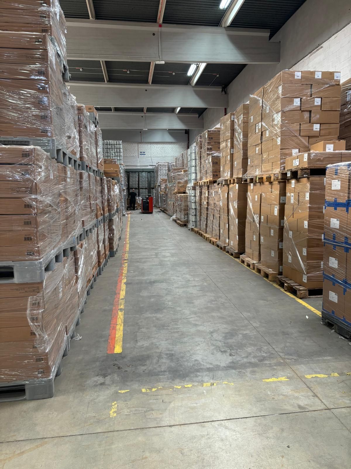 Lagergang mit gestapelten Kartons auf Paletten, in Plastik eingewickelt.