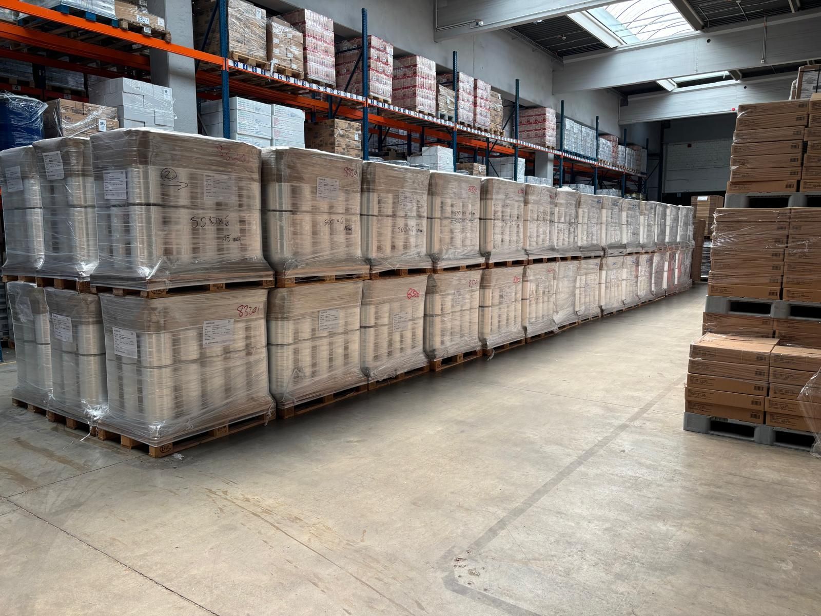 Lagerinnenraum mit Stapeln verpackter Waren auf Paletten. Im Hintergrund sind Regale gestapelt.