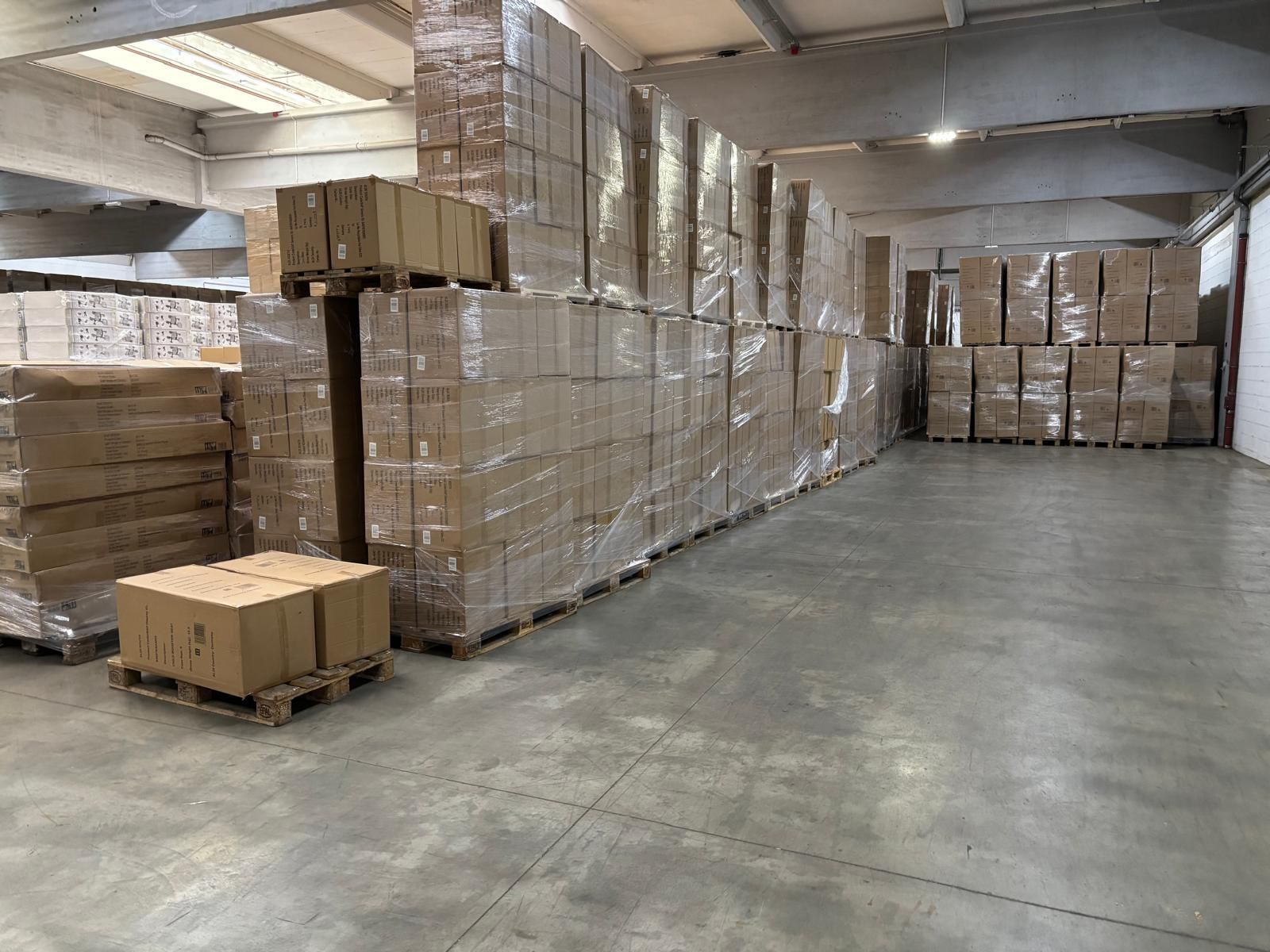 Lagerinnenraum mit Stapeln von Kartons auf Holzpaletten, eingewickelt in durchsichtige Plastikfolie.