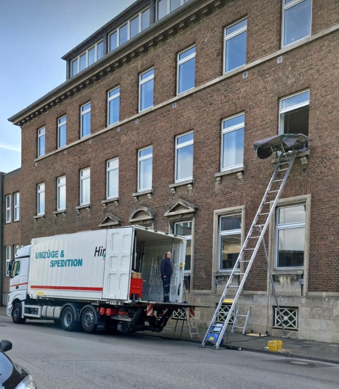 Umzugswagen vor einem verklinkerten Haus mit einer Hebebühne an ein Fenster
