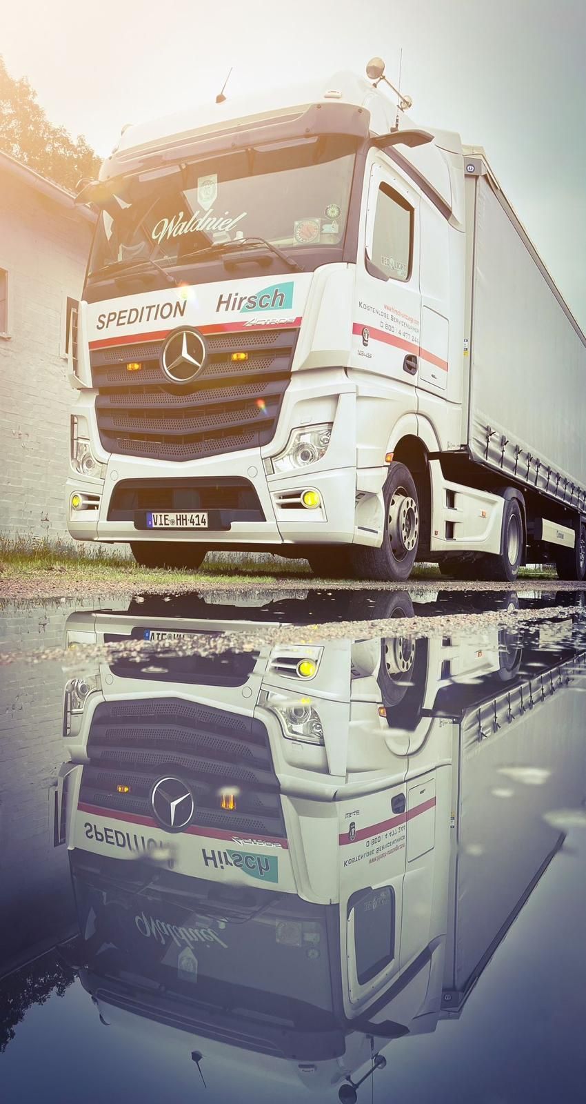 Weißer Sattelschlepper spiegelt sich an einem bewölkten Tag in einer Pfütze.