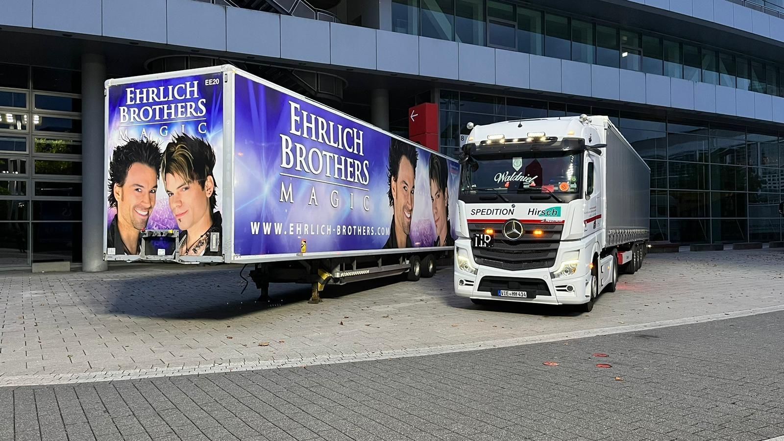 Ein weißer Sattelschlepper mit Anhänger und der Aufschrift „Ehrlich Brothers“ parkte in der Nähe eines Gebäudes.