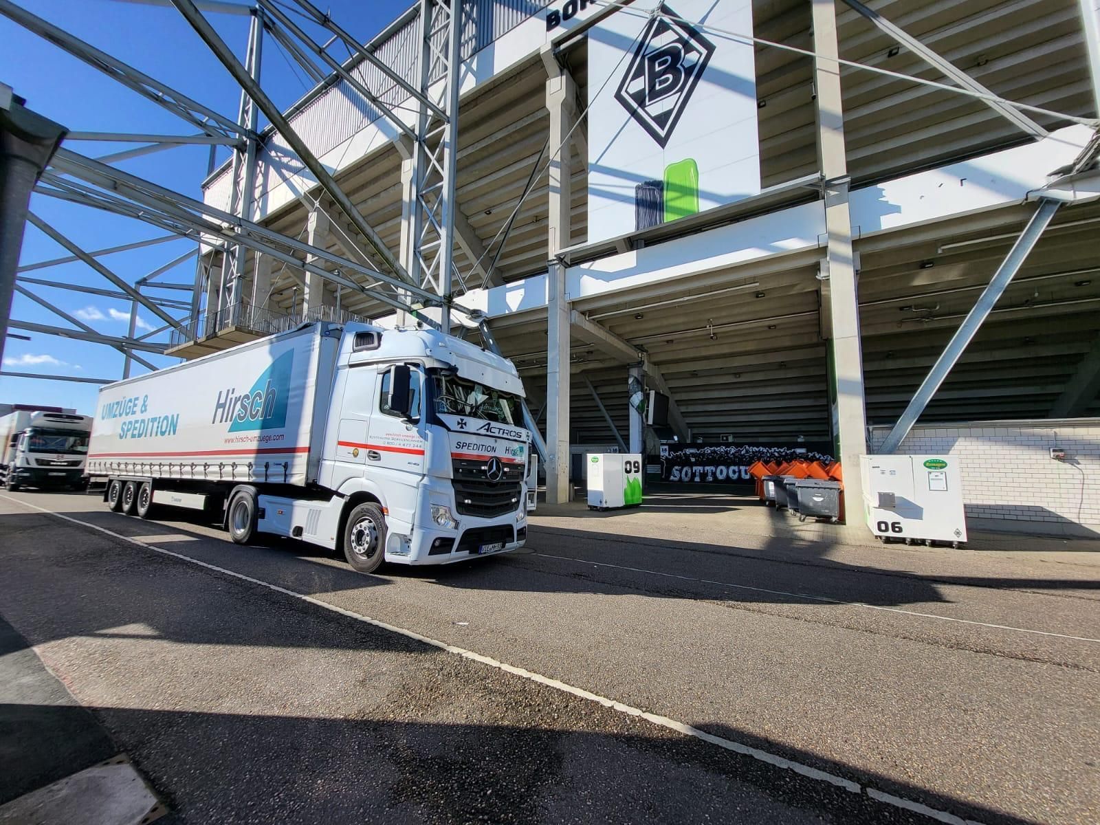 Vor einem Stadioneingang parkt ein weißer Lastwagen mit einem Logo.