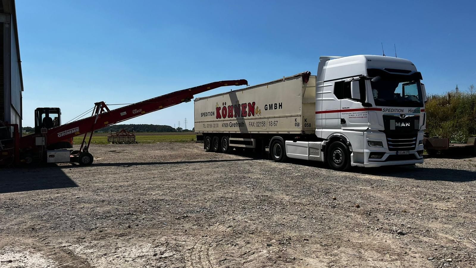 Ein LKW wird mit einem Erdbohrer beladen. Blauer Himmel, Schotterboden. „ROBINSON“-Logo auf dem Anhänger.